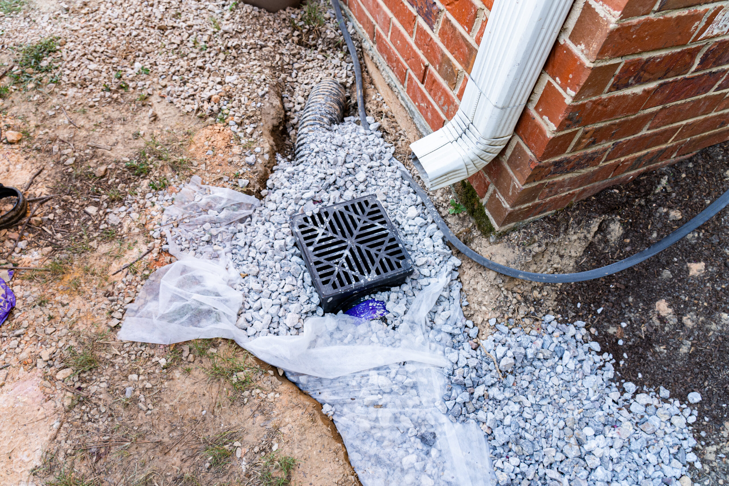 Plastic catch basin installed under a downspout to alleviate drainage issues against a red brick home